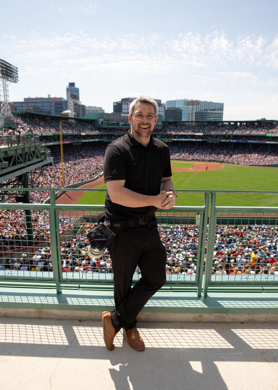 Eric smiling, leaning on a railing with a camera on his hip